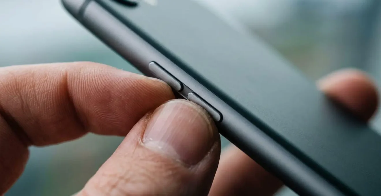 Macro photograph of fingers pressing physical buttons on the side of a smartphone with shallow depth of field, emphasizing the tactile action of activating emergency lockdown