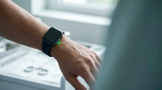 Close-up photograph of smartwatch optical sensor glowing on human wrist in soft natural lighting representing medical health monitoring technology